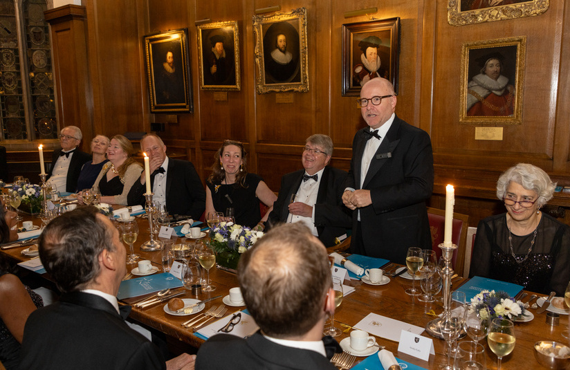 A photo of a person standing at a dinner table addressing the room in a speech