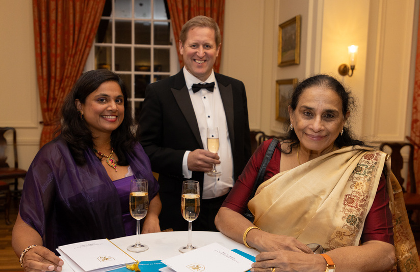 A photo of two people sitting at a table and one person behind them - all drinking champagne