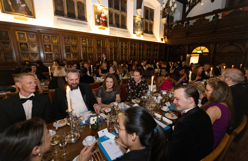 A wide photo of about 30 to 50 people sitting at long dinner tables 