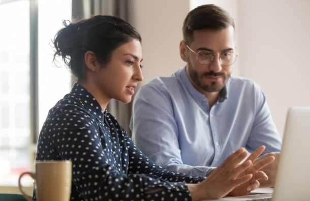 A woman and a man sitting in front of a laptop, the woman explaining something