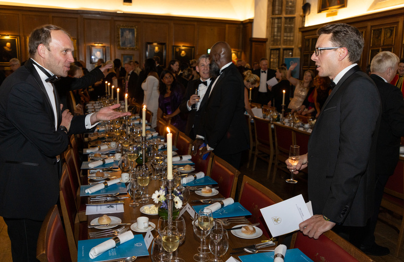 A photo of people standing around a long dinner table that has brochures and dinner place settings