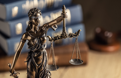 A photo of a statue of lady justice in the foreground and legal books in the background