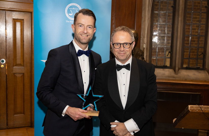 A photo of Chris Loweth with his award standing with another person 