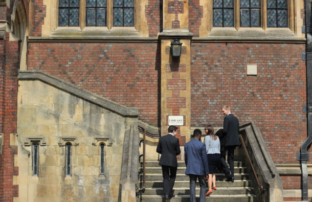 Four people, pupils, climbing external stairs towards an old building, with a library sign out the front