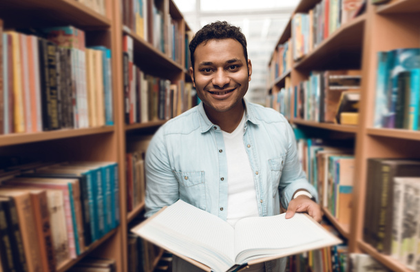 A pupil holding an open book inbetween bookshelves.